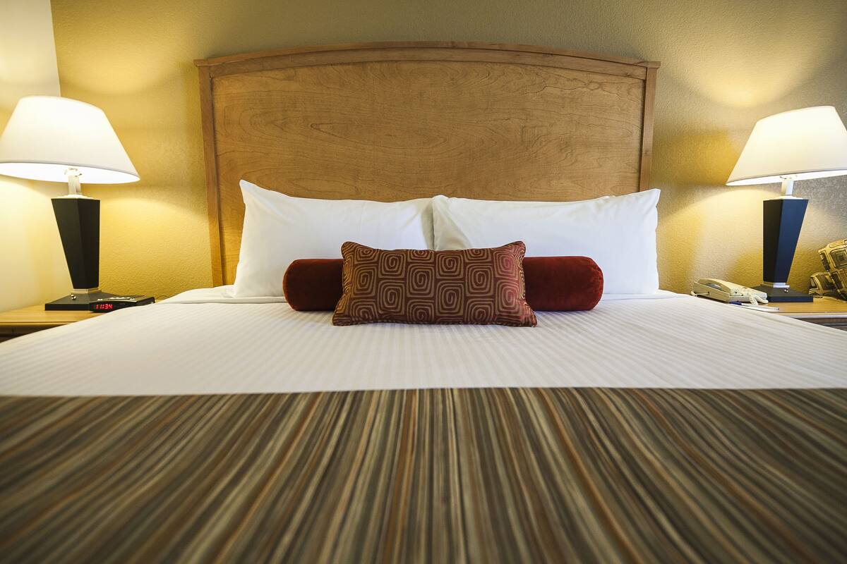 Ein Hotelzimmer mit einem großen Bett, zwei Nachttischlampen, einem hölzernen Kopfteil und einem Nachttisch mit Telefon und Wecker.