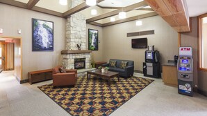 A lobby with a fireplace, a sofa, a coffee table, an ATM, and a patterned rug. - Mountain Retreat Hotel (Squamish)