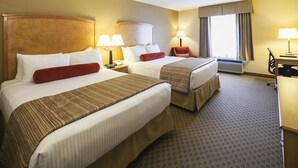 A hotel room with two beds, each with a headboard, bedside tables with lamps, a desk with a chair, and a large window with curtains. - Mountain Retreat Hotel (Squamish)