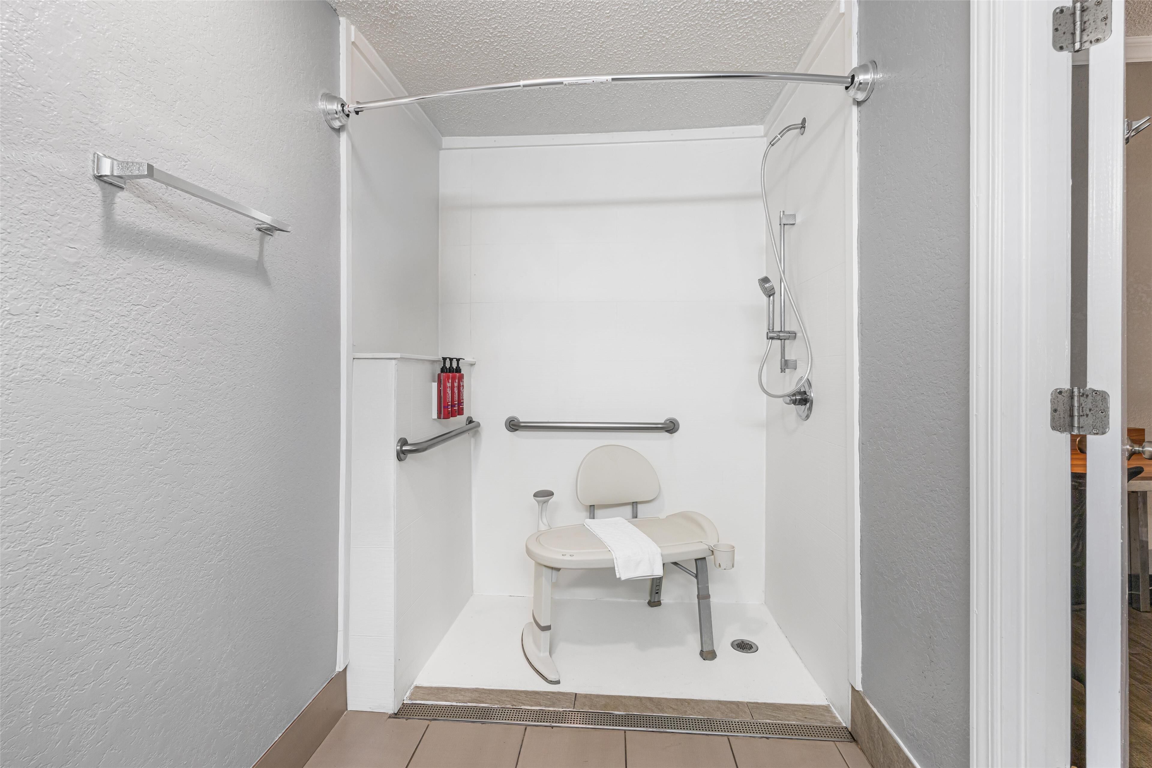 Cabina de ducha accesible en silla de ruedas, con barra de apoyo, una toalla y un cabezal de ducha de mano.