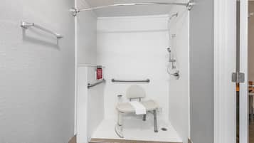 Cabina de ducha accesible en silla de ruedas, con barra de apoyo, una toalla y un cabezal de ducha de mano.