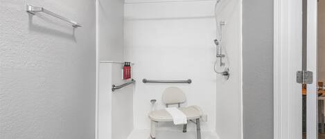 Cabina de ducha accesible en silla de ruedas, con barra de apoyo, una toalla y un cabezal de ducha de mano.