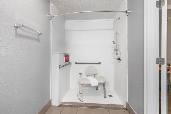 Cabina de ducha accesible en silla de ruedas, con barra de apoyo, una toalla y un cabezal de ducha de mano.