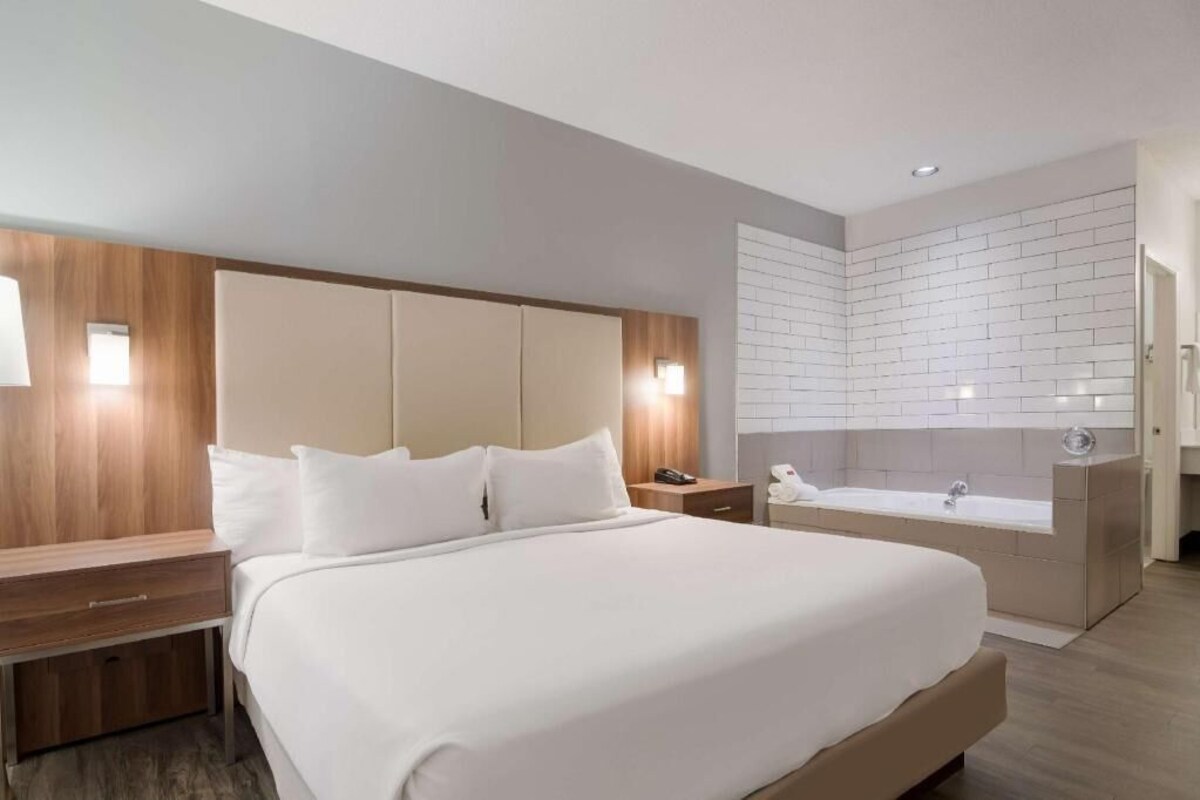 Une chambre d’hôtel moderne dotée d’un grand lit, d’une coiffeuse intégrée avec un miroir et d’une salle de bain séparée avec une baignoire.