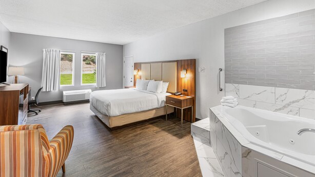 Une chambre d’hôtel comprenant un lit, un bureau, une chaise, une salle de bain avec baignoire et une vue sur la verdure.