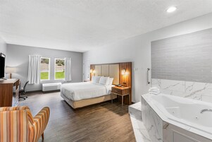 Habitación de hotel con cama, escritorio, silla, baño con bañera y vistas a zonas verdes.