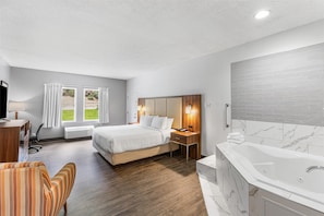 Habitación de hotel con cama, escritorio, silla, baño con bañera y vistas a zonas verdes.