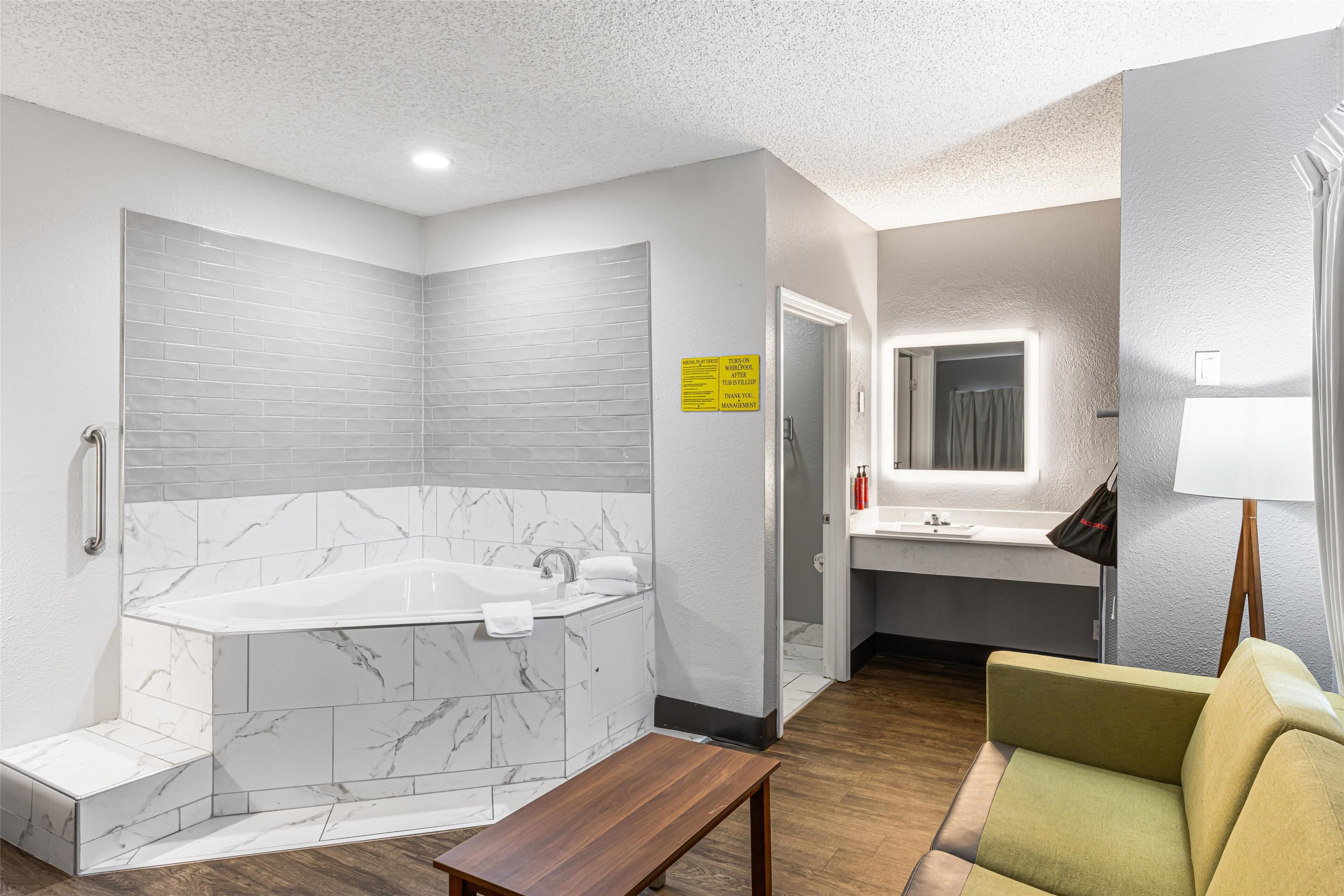 A modern bathroom with a large bathtub, a vanity with a mirror, and a bench.