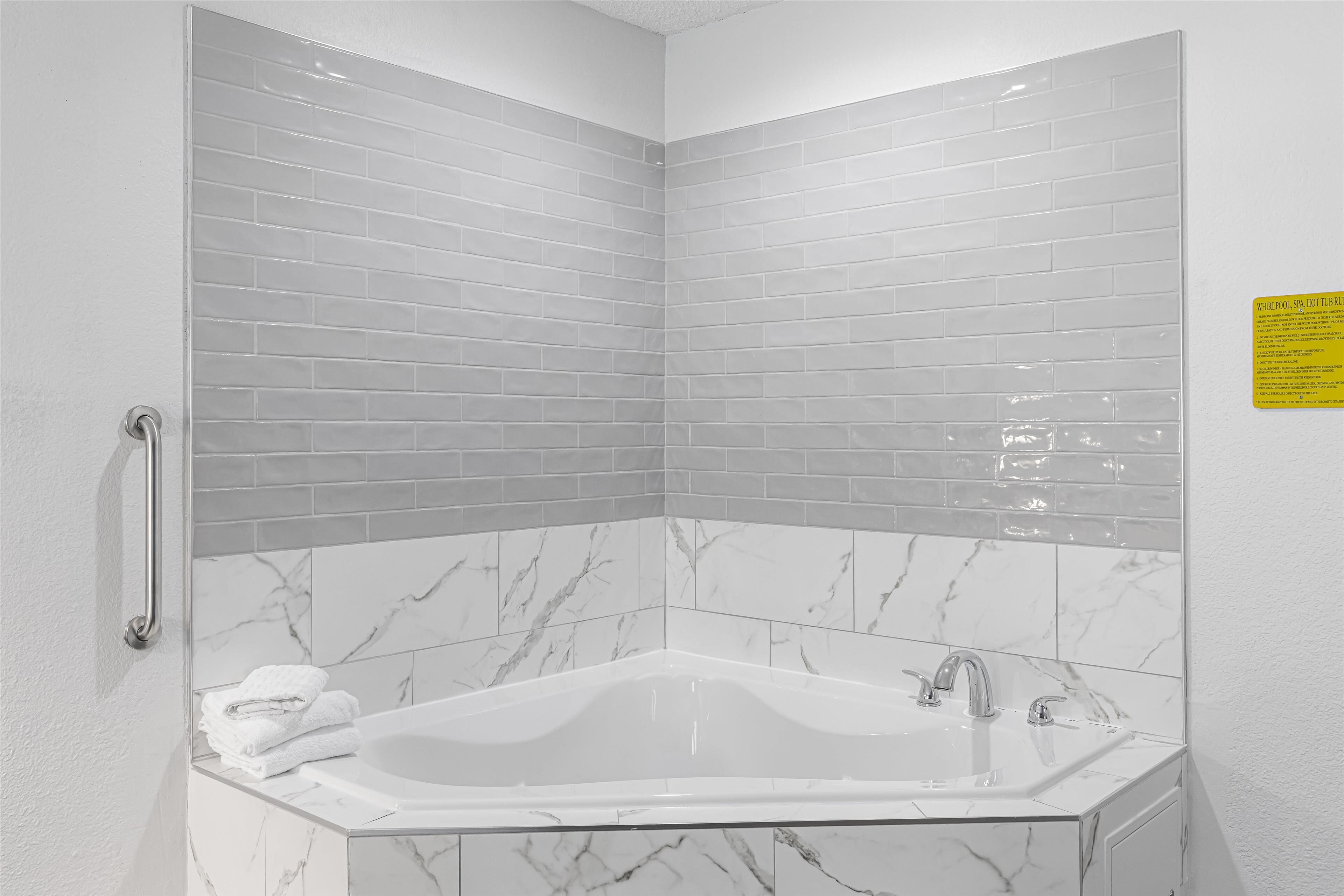 A corner bathroom with a white marble sink, a bathtub, and grey subway tiles.