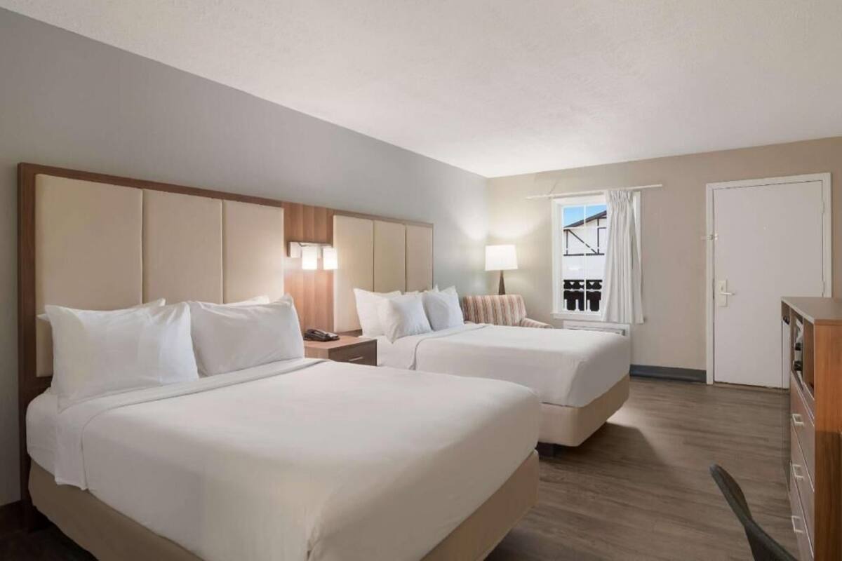 Ein Hotelzimmer mit zwei Betten, einem Schreibtisch, einer Lampe, einem Kleiderschrank und einem Fenster mit Vorhängen.