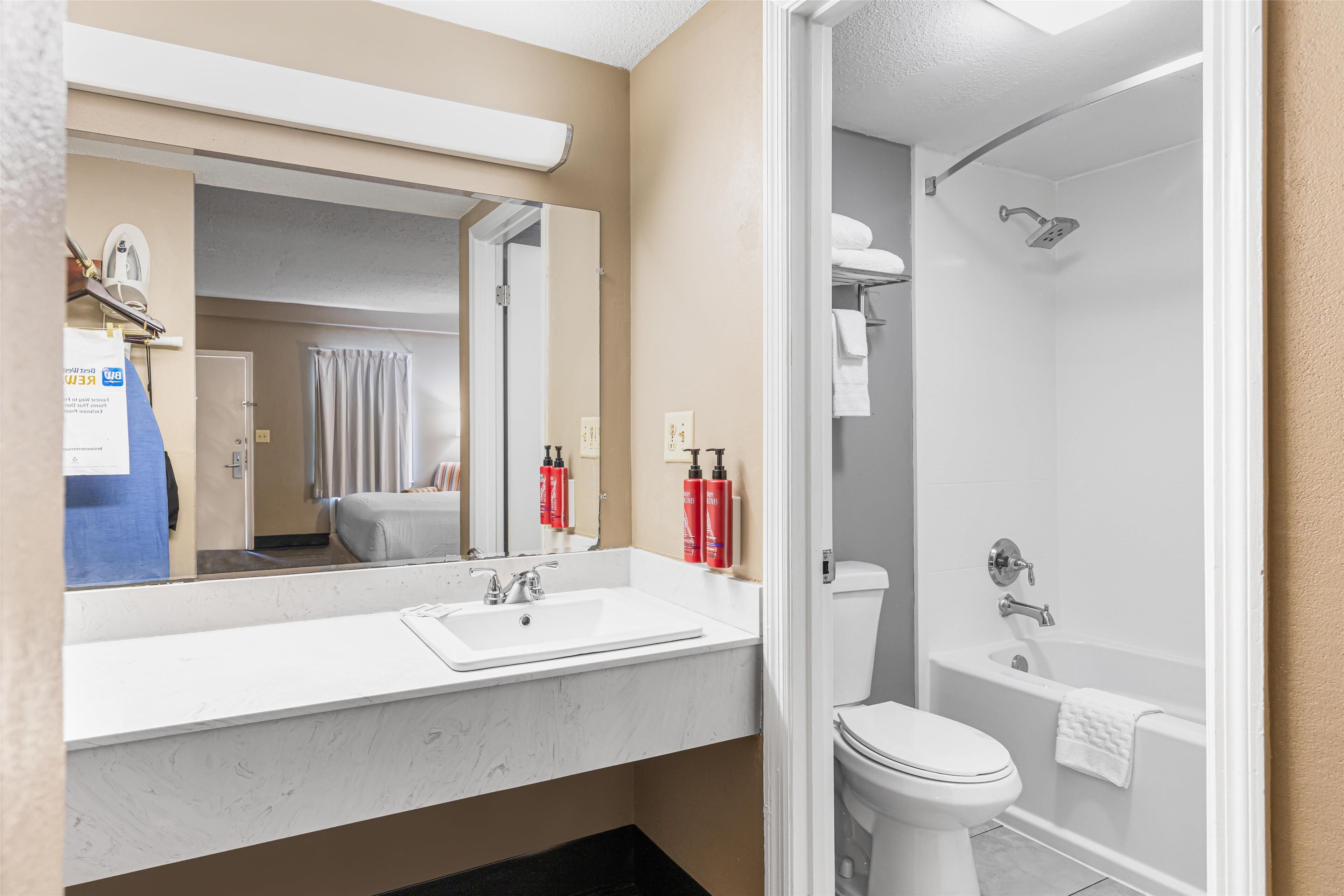 Une salle de bain moderne avec un lavabo blanc, un miroir et des toilettes. Il y a un espace douche avec une baignoire et une serviette accrochée au mur.