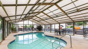 Une piscine intérieure dotée d’un toit en verre, entourée de chaises longues et offrant une vue sur l’extérieur.