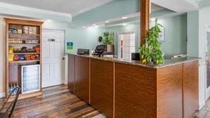 Un espace d’accueil avec un comptoir en bois, un réfrigérateur rempli de collations et une plante en pot.