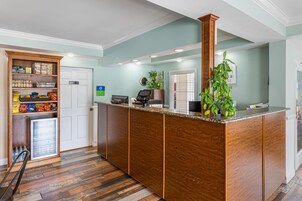 Una zona de recepción con un mostrador de madera, un refrigerador lleno de aperitivos y una planta en maceta.