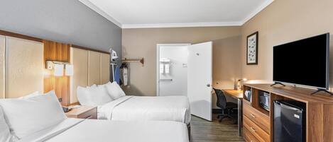 Et hotelværelse med to senge, et skrivebord, et fjernsyn og et køleskab.