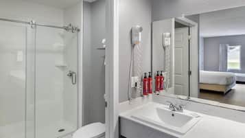 Une salle de bain moderne avec une douche à l’italienne en verre, un lavabo blanc et un grand miroir.