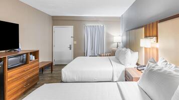 Habitación de hotel con dos camas, televisión, cómoda de madera, escritorio con lámpara y puerta de baño.