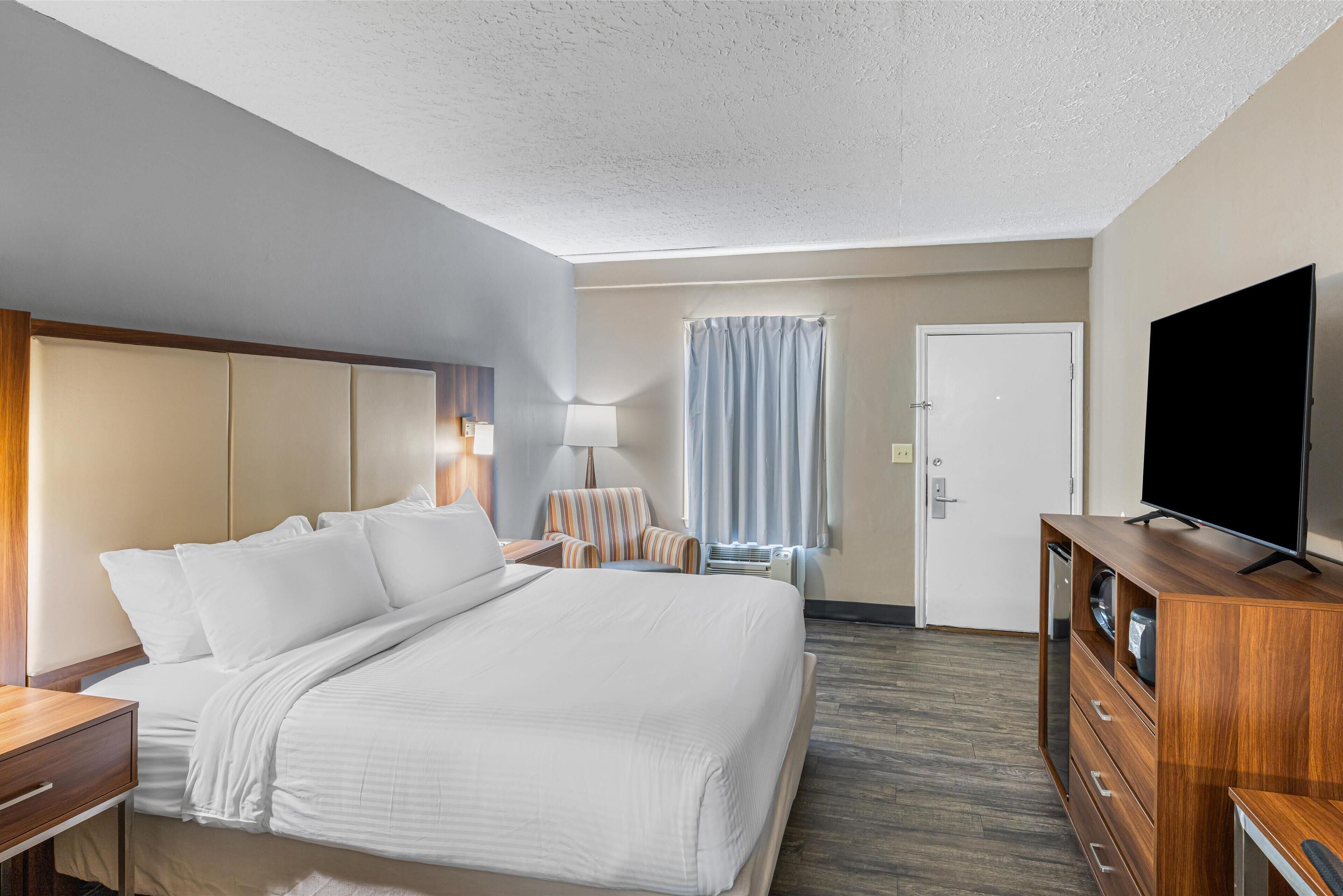 Ein Hotelzimmer mit einem großen Bett, einem Holzkoffer, einem Fernseher, einem Schreibtisch und einem Sessel.