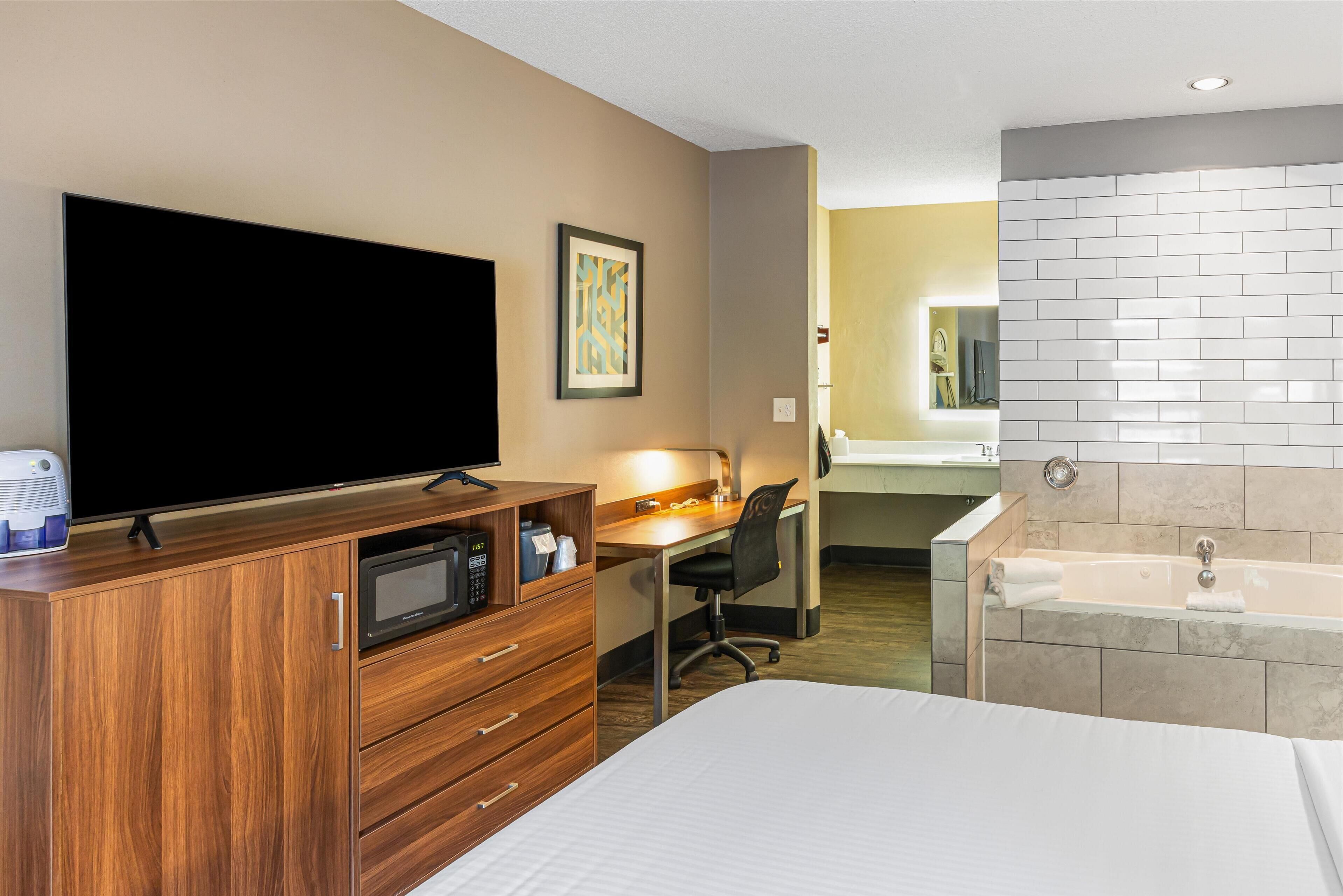 Habitación de hotel con cama, escritorio y silla, televisor, microondas, lavamanos y bañera.
