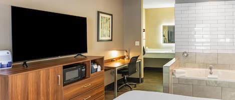 Habitación de hotel con cama, escritorio y silla, televisor, microondas, lavamanos y bañera.
