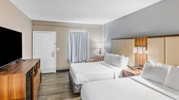 A hotel room with two beds, a TV, a desk, and a mirror.