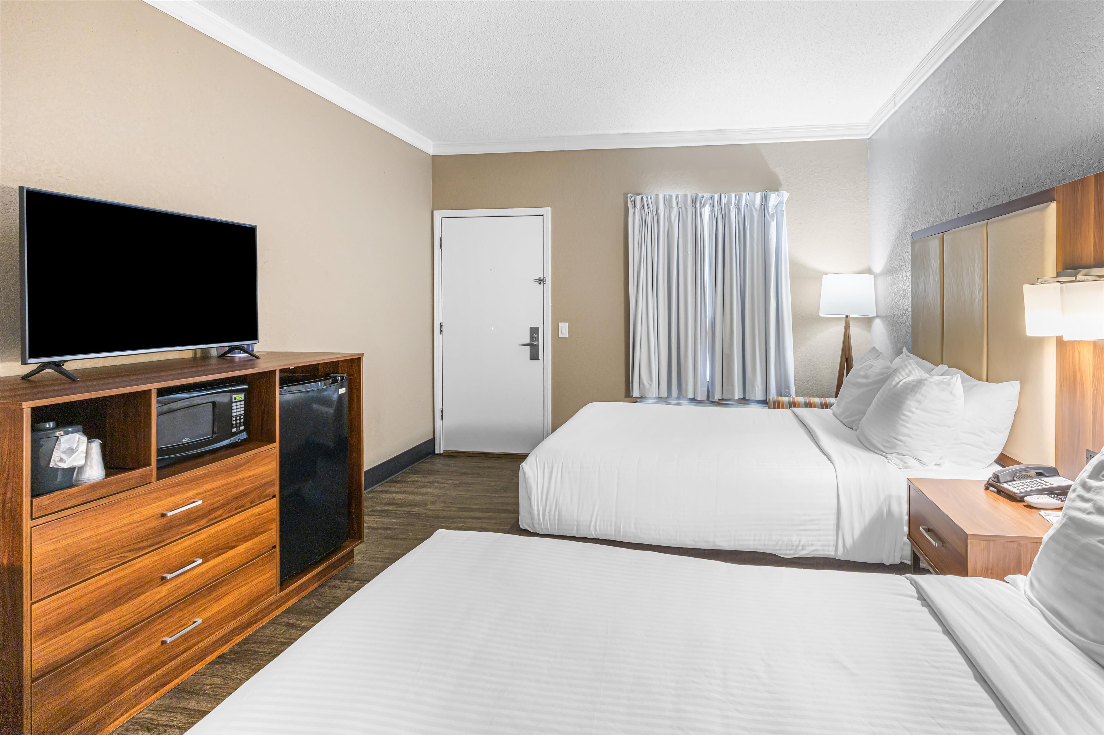 A hotel room with a large bed, a TV, a minibar, and a door.