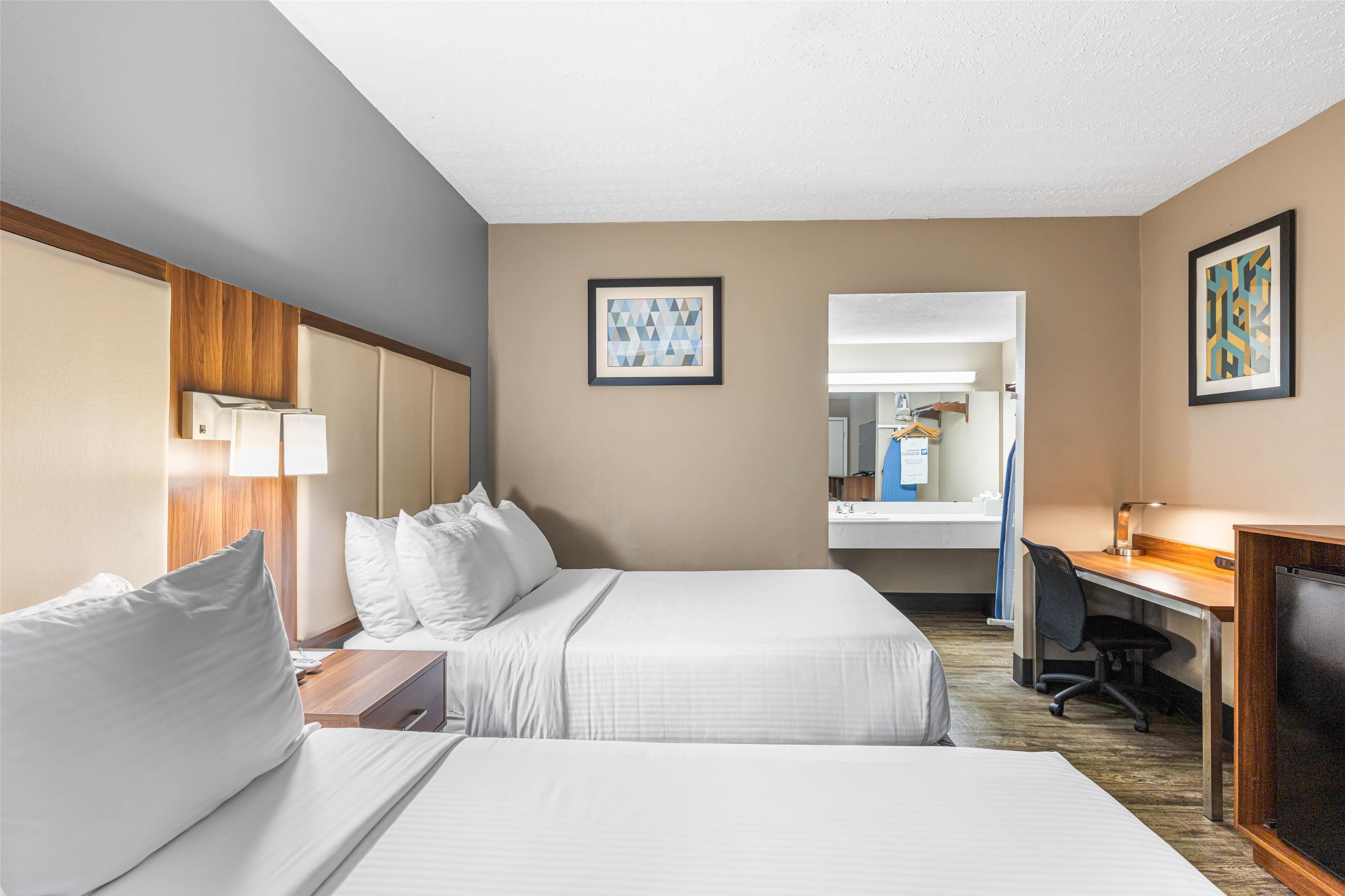 Une chambre d’hôtel avec deux lits, un bureau, une chaise, une télévision et un miroir.
