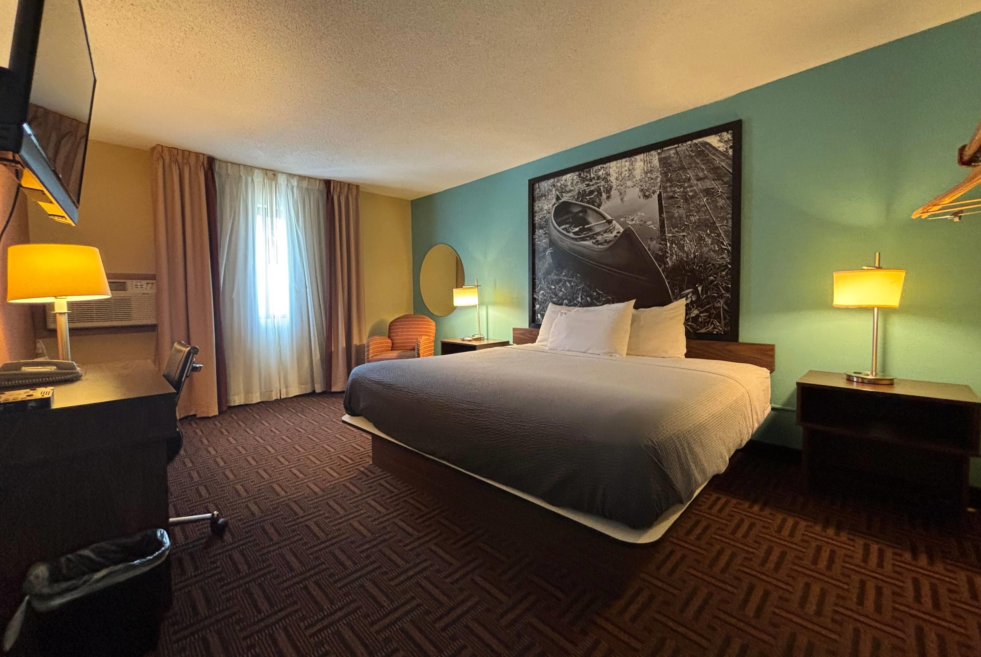 A hotel room with a large bed, two bedside tables with lamps, a desk with a telephone, a chair, and a window with curtains.