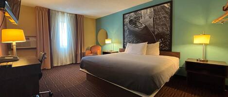 A hotel room with a large bed, two bedside tables with lamps, a desk with a telephone, a chair, and a window with curtains.