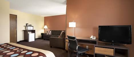 A hotel room with a bed, a desk with a computer, a TV, a chair, a lamp, and a minibar.