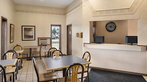 Un hall d’hôtel avec un comptoir d’accueil, plusieurs tables et chaises, des tableaux encadrés aux murs et une horloge.