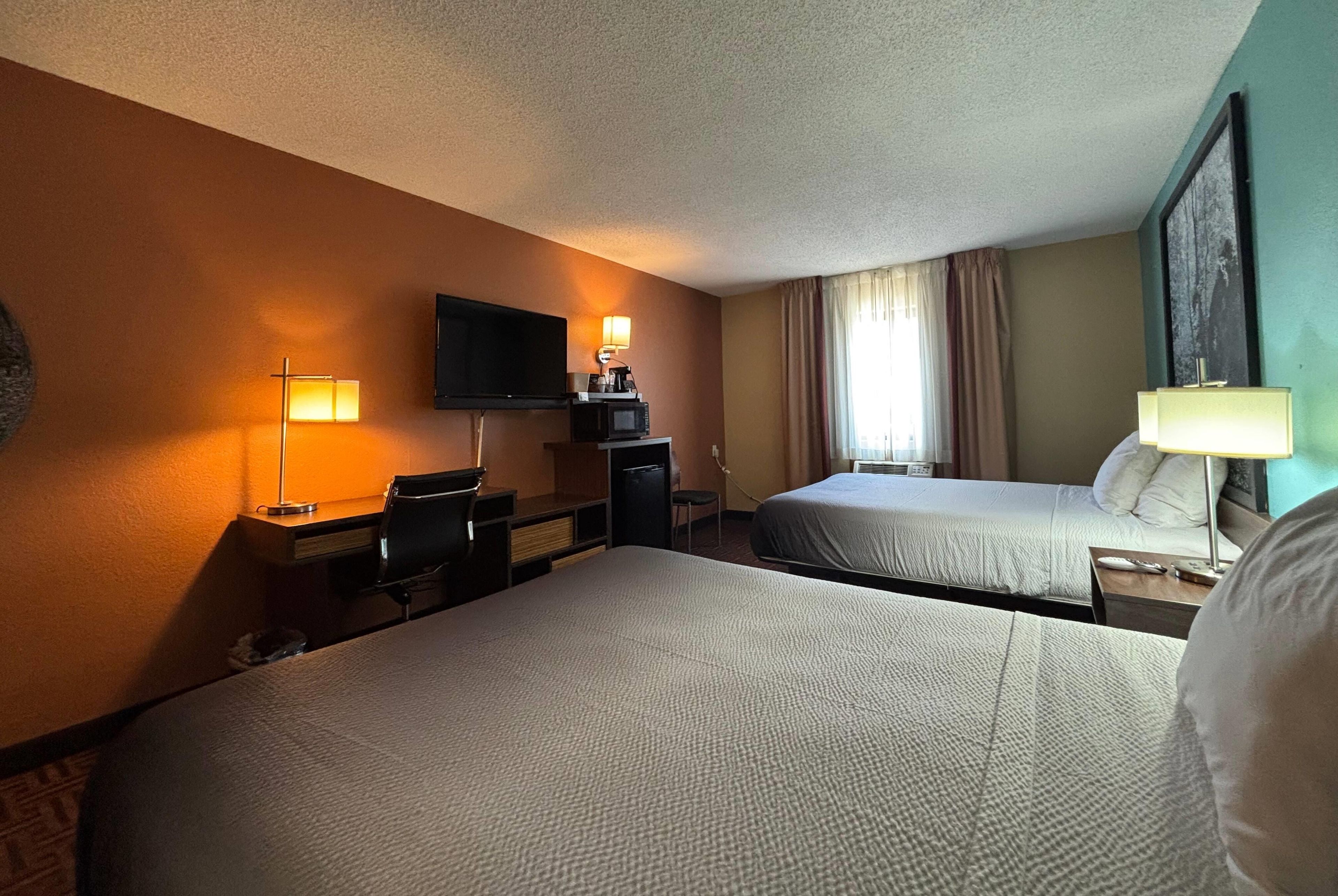 A hotel room with two beds, a desk with a chair, a television, and a window with curtains.
