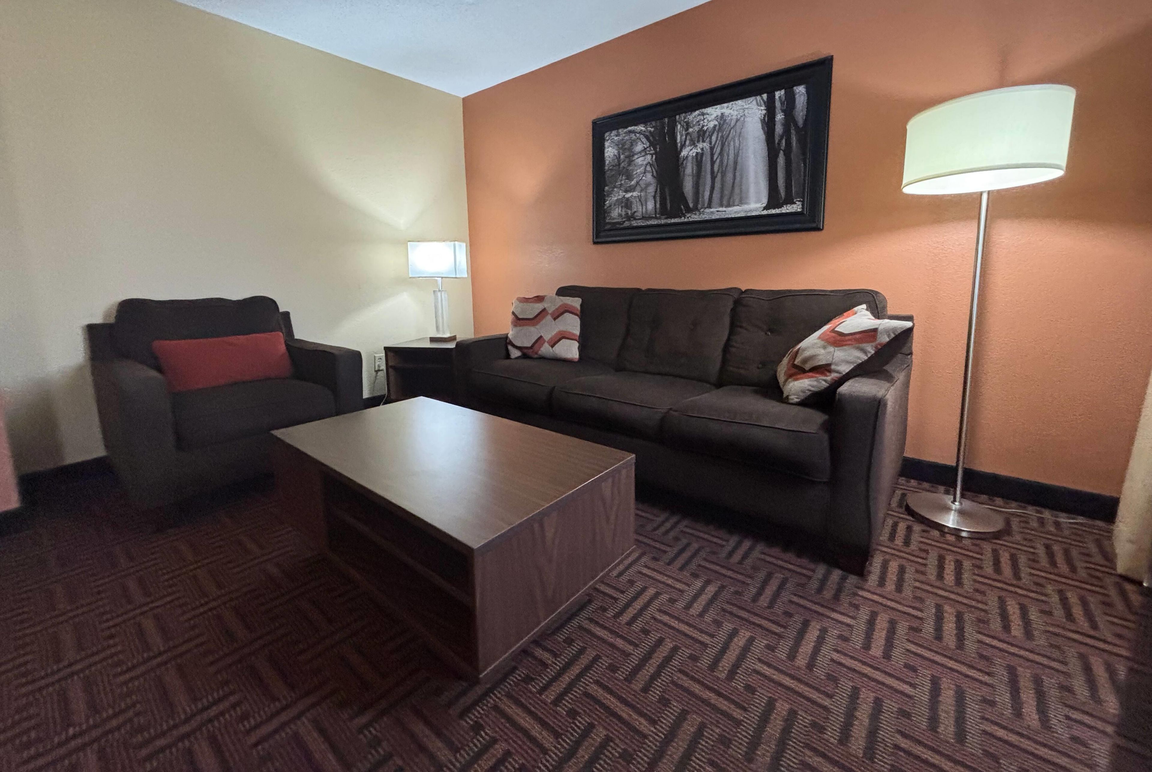 A hotel room with a sofa, a coffee table, a floor lamp, and a painting on the wall.