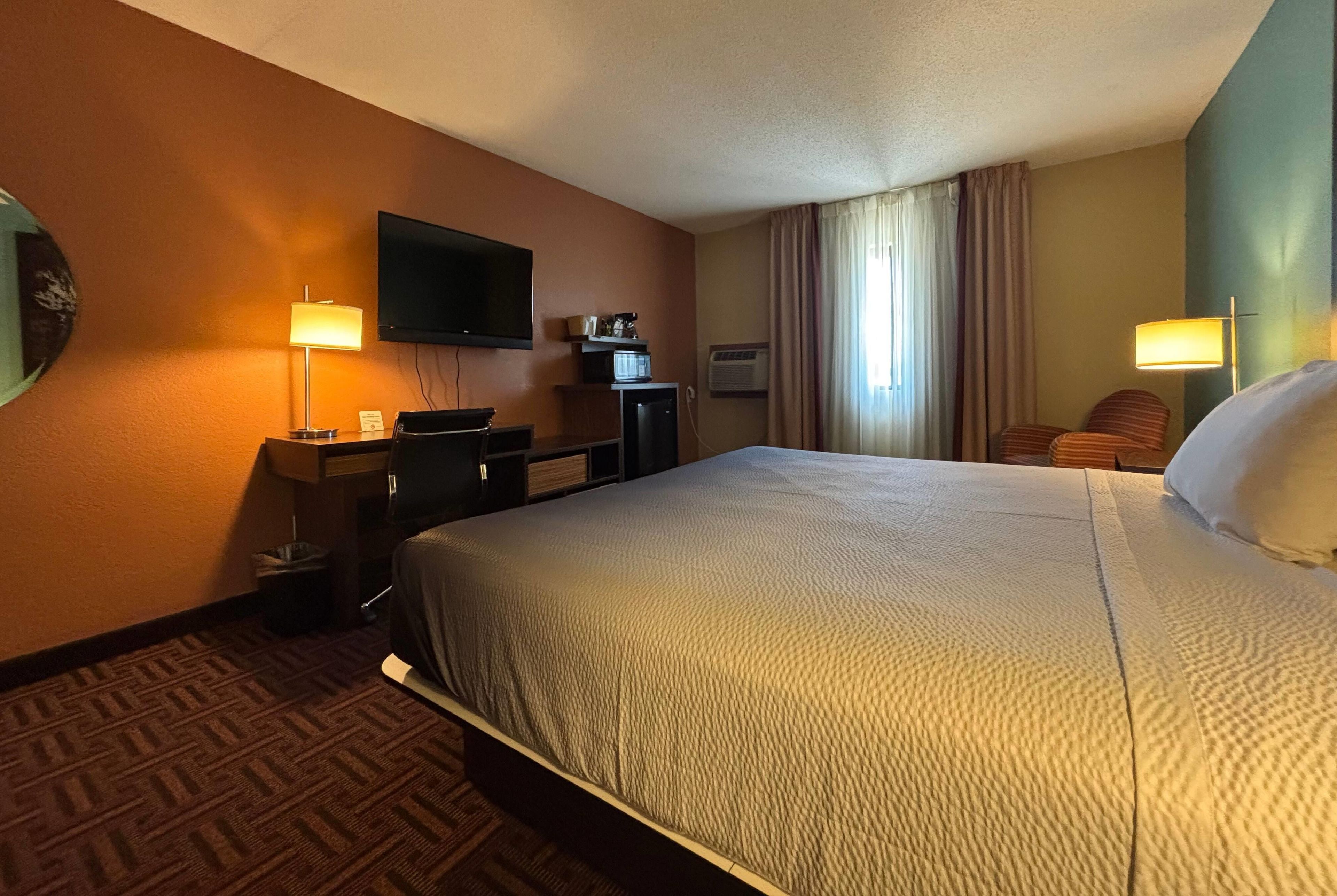 A hotel room with a bed, a desk, a television, and a window with curtains.