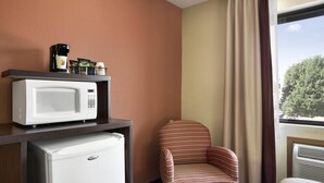 Une chambre d’hôtel équipée d’un four à micro-ondes, d’un réfrigérateur, d’une chaise et d’une fenêtre avec des rideaux.