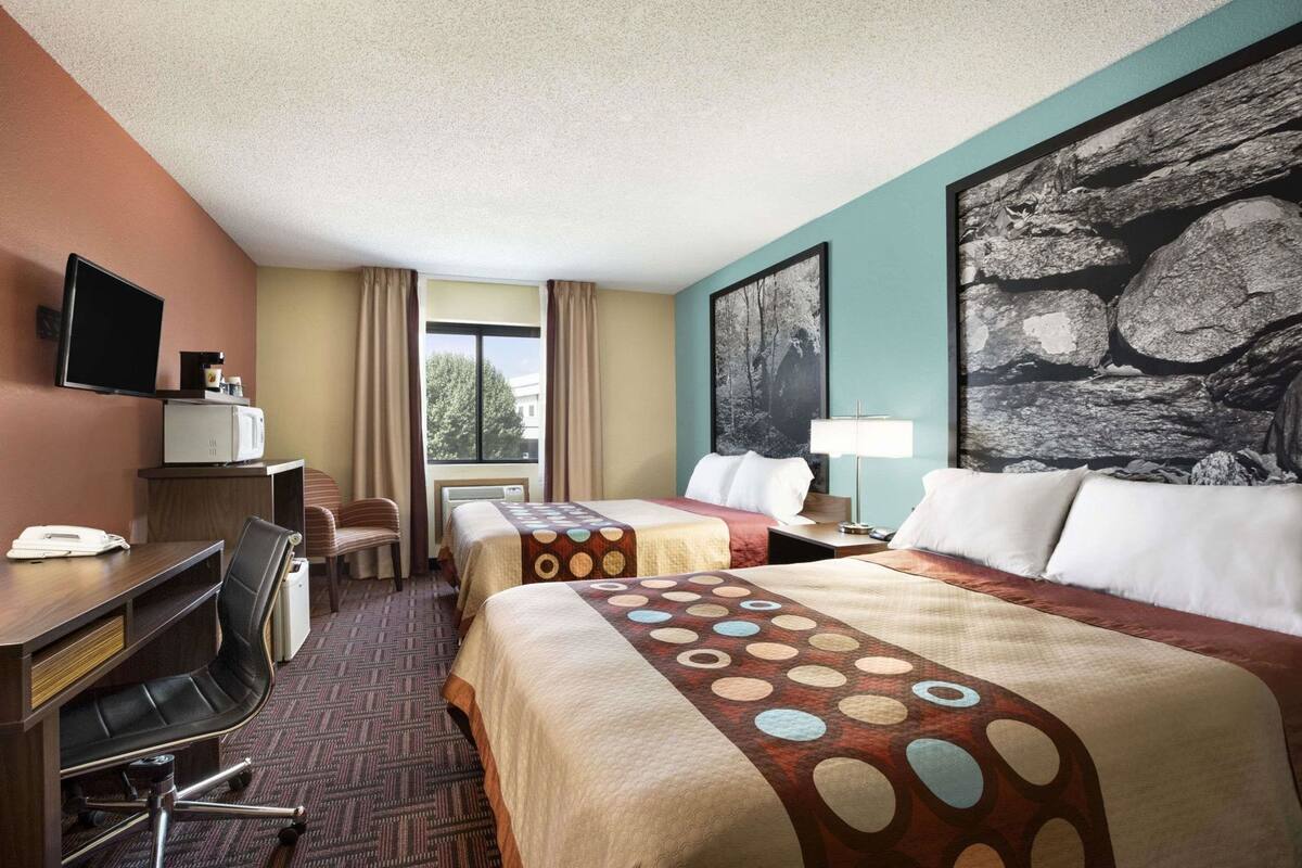 A hotel room with two beds, a desk with a chair, a television, and a window with curtains.