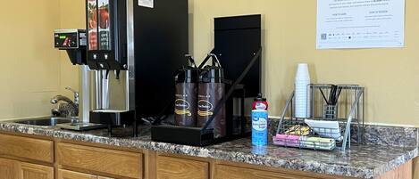 A coffee station with a coffee machine, sugar dispensers, and a cup holder.