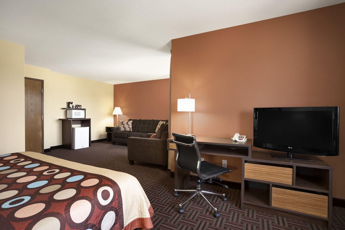 A hotel room with a bed, a desk with a TV, a chair, a sofa, a lamp, and a small refrigerator.