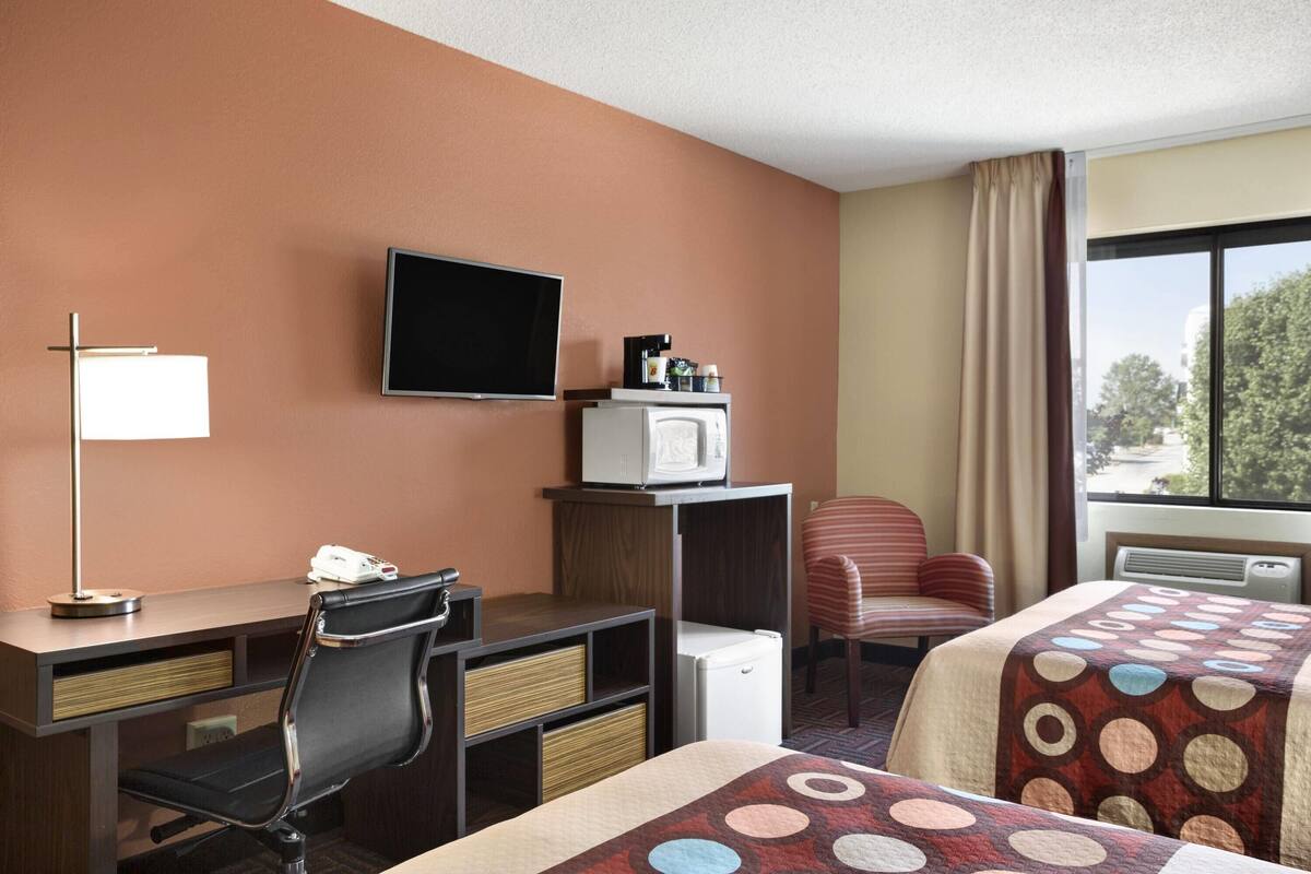 A hotel room with a desk, chair, television, microwave, and two beds with patterned bedspreads.