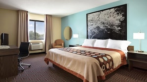 Une chambre d’hôtel avec un grand lit, un bureau, une chaise, une fenêtre avec des rideaux, un téléviseur fixé au mur et un grand tableau.