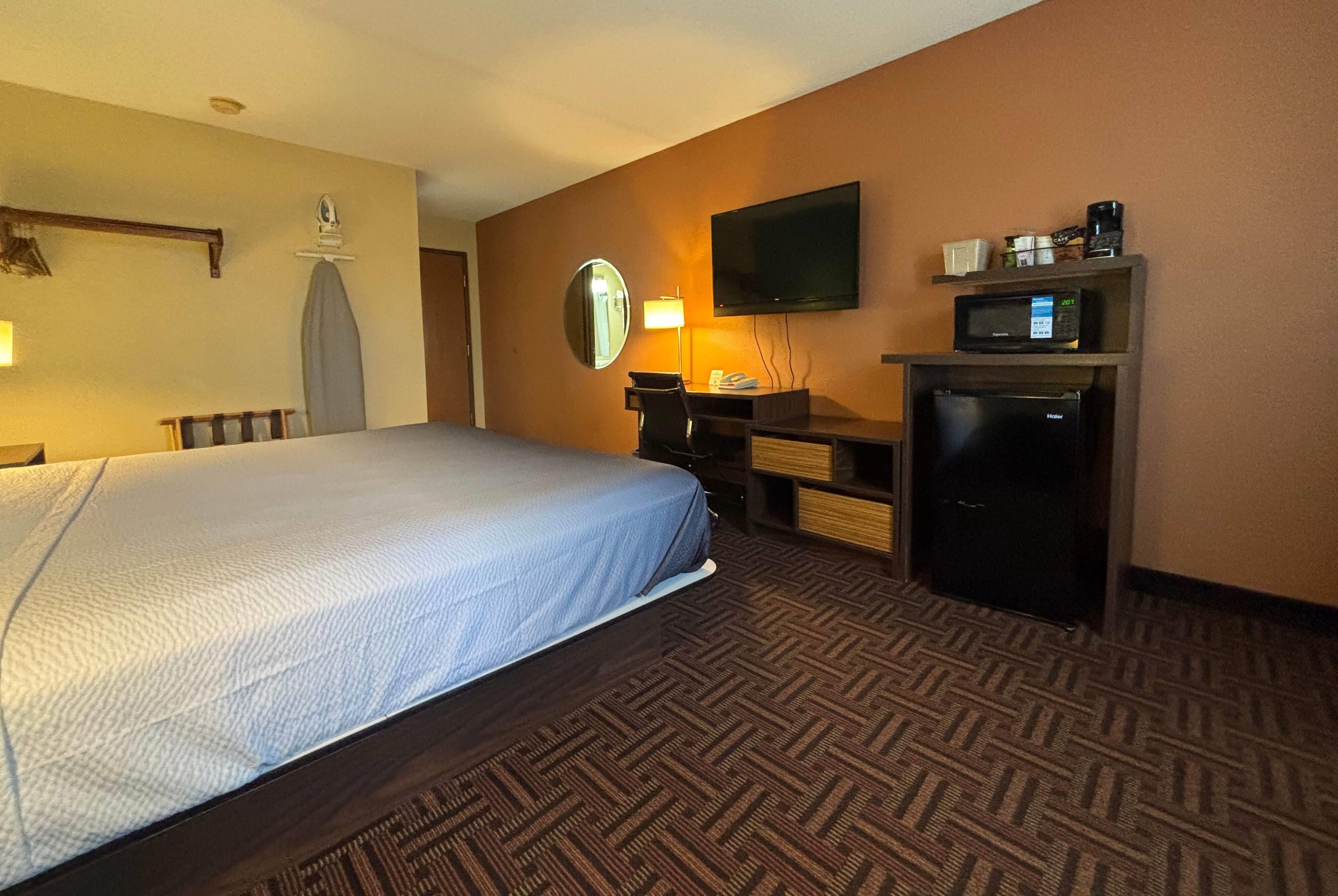 Habitación de hotel con cama, escritorio, televisor de pantalla plana, microondas y refrigerador pequeño.