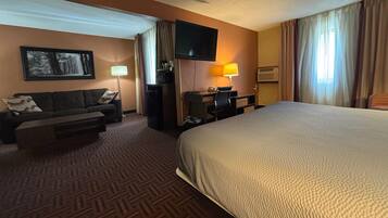 A hotel room with a bed, a sofa, a desk, a TV, and a painting on the wall.