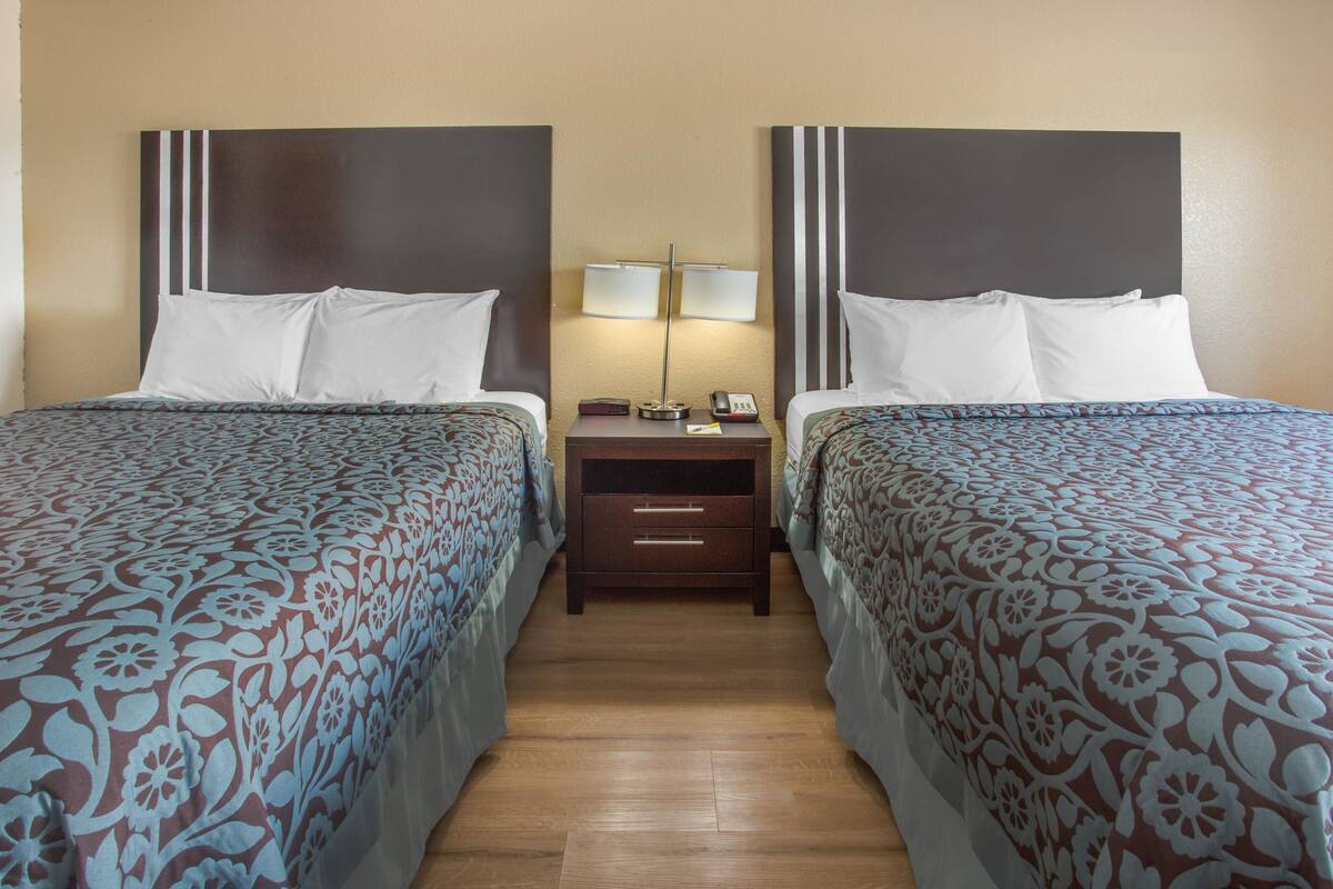 A hotel room with two beds, each with a patterned bedspread, a nightstand with a lamp, and a drawer.