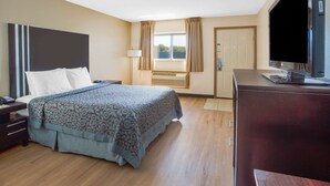 A hotel room with a bed, bedside table, lamp, TV, and a window with curtains. - Days Inn by Wyndham Le Roy/Bloomington Southeast (Le Roy)