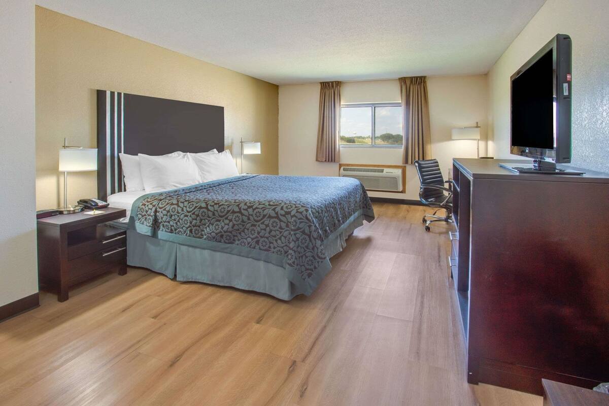 A hotel room with a bed, bedside tables, a desk, a chair, a television, and a window with curtains.