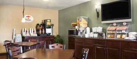 Un rincón para desayunar con mesas y sillas, una estación de café y un televisor montado en la pared.