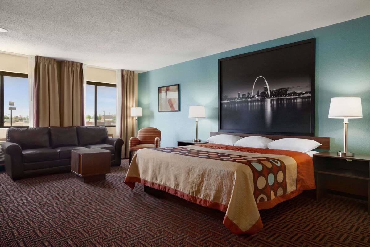 Una habitación de hotel con cama, sofá, silla, escritorio y lámpara.