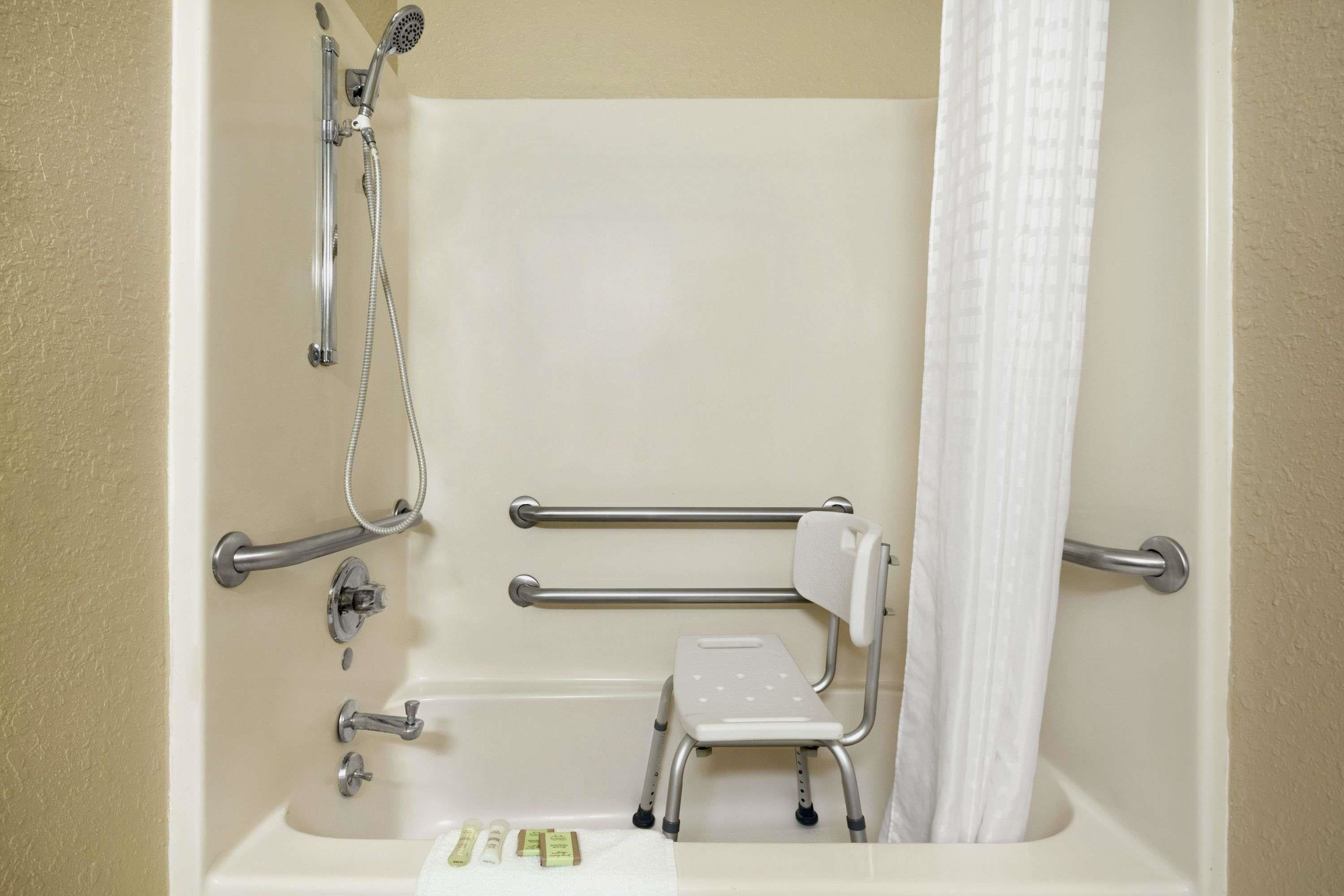A bathroom with a bathtub, grab bars, a showerhead, a step stool, and a towel rack.