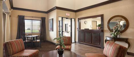 A lobby with striped armchairs, a round table with a plant, and a mirror on the wall.