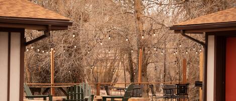Un espacio al aire libre con bancos y sillas de madera, rodeado de árboles y luces colgantes.